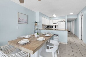 A modern kitchen with white cabinets, a wooden dining table, and white chairs. - Palms Resort 501: 3BR Oceanfront Condo (Myrtle Beach)