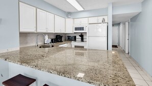 Una cocina moderna con armarios blancos, encimeras de granito, un microondas y un lavabo.