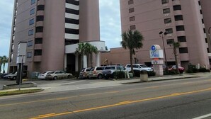 Two tall, pink-colored buildings with a central entrance and a parking area in front. - Palms Resort 501: 3BR Oceanfront Condo (Myrtle Beach)