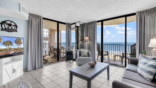 A modern hotel room with a balcony, a dining area, and a TV. - Palms Resort 501: 3BR Oceanfront Condo (Myrtle Beach)
