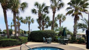 A pool area with a circular pool, surrounded by palm trees and a hedge. - Palms Resort 501: 3BR Oceanfront Condo (Myrtle Beach)