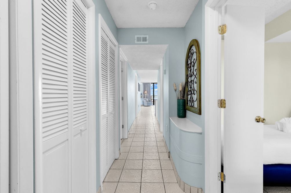 A hotel hallway with white doors, a tiled floor, and a bed with a blue headboard.
