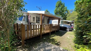 A mobile home with a deck and a car parked nearby. - MOBILHOME 6 PERS CAMPING 3 Stars near the sea (Lunel)