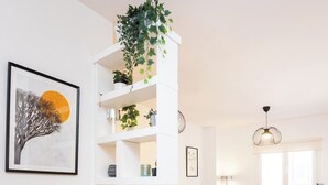 Una sala de estar moderna con un estante blanco, una mesita de mimbre, un sofá gris, dos sillones y una lámpara de pie.