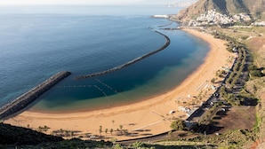 Un pueblo costero con una playa, un muelle largo y una montaña al fondo.
