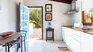 A kitchen with a wooden table, a blue door, a small side table with a lamp, and a toaster on the counter.