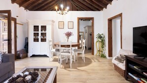 A spacious living room with a wooden ceiling, a dining area with a round table and chairs, a sofa, a TV stand, and a bookshelf.
