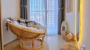 A room with a wicker chair, a woven mat, a wall-mounted macrame decoration, and a small basket with magazines.
