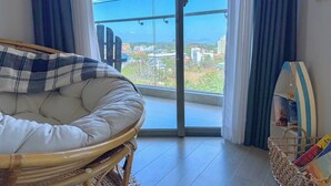 A room with a large window, a wicker chair, a cushioned bench, and a small table with a basket.