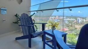 A balcony with a mesh screen, a blue Adirondack chair, a small table, and a potted plant.