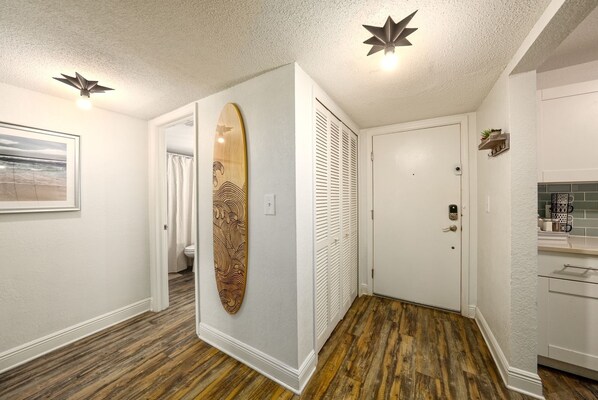 Een gang met een houten surfboard, een deur en een keukenhoek met aanrecht en kasten.
