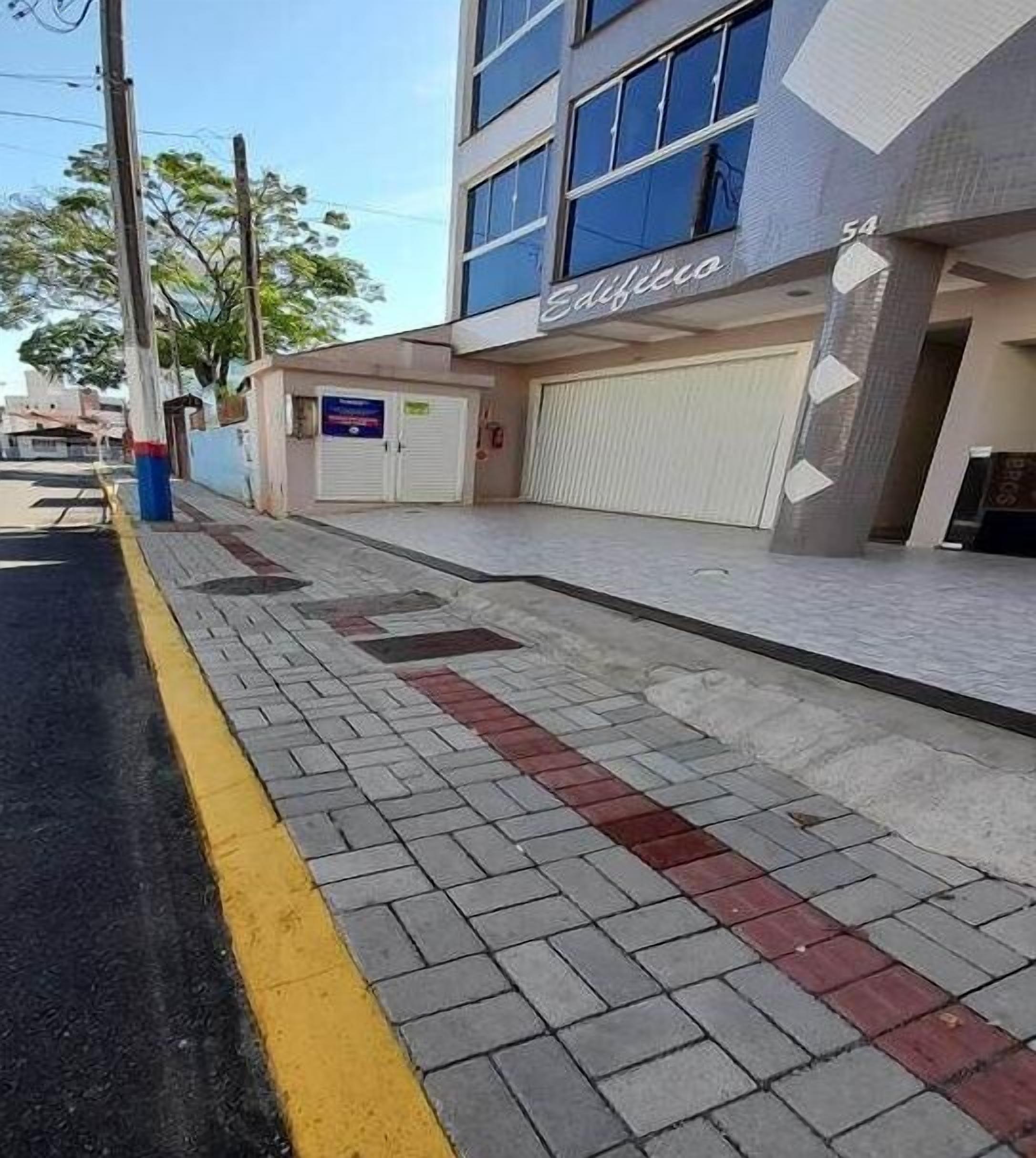 Una acera con bordillo amarillo, un edificio con persiana cerrada y un cartel que dice 'Edificio'.