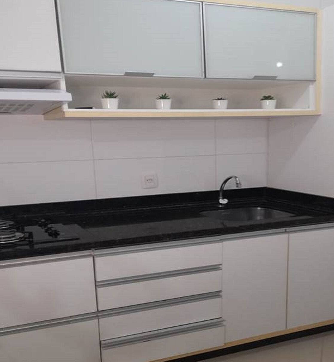 A kitchen with white cabinets, a black countertop, a sink, and a stove.