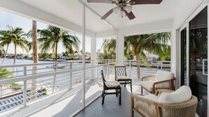 A balcony with wicker furniture, a ceiling fan, and a view of palm trees and water. - Boca Waterfront Oasis: Bright Corner Unit – Walk to Beach (Boca Raton)