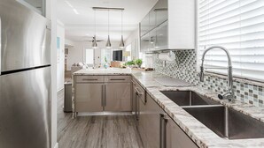 A modern kitchen with a stainless steel refrigerator, a marble countertop, and a sink with a faucet. - Boca Waterfront Oasis: Bright Corner Unit – Walk to Beach (Boca Raton)