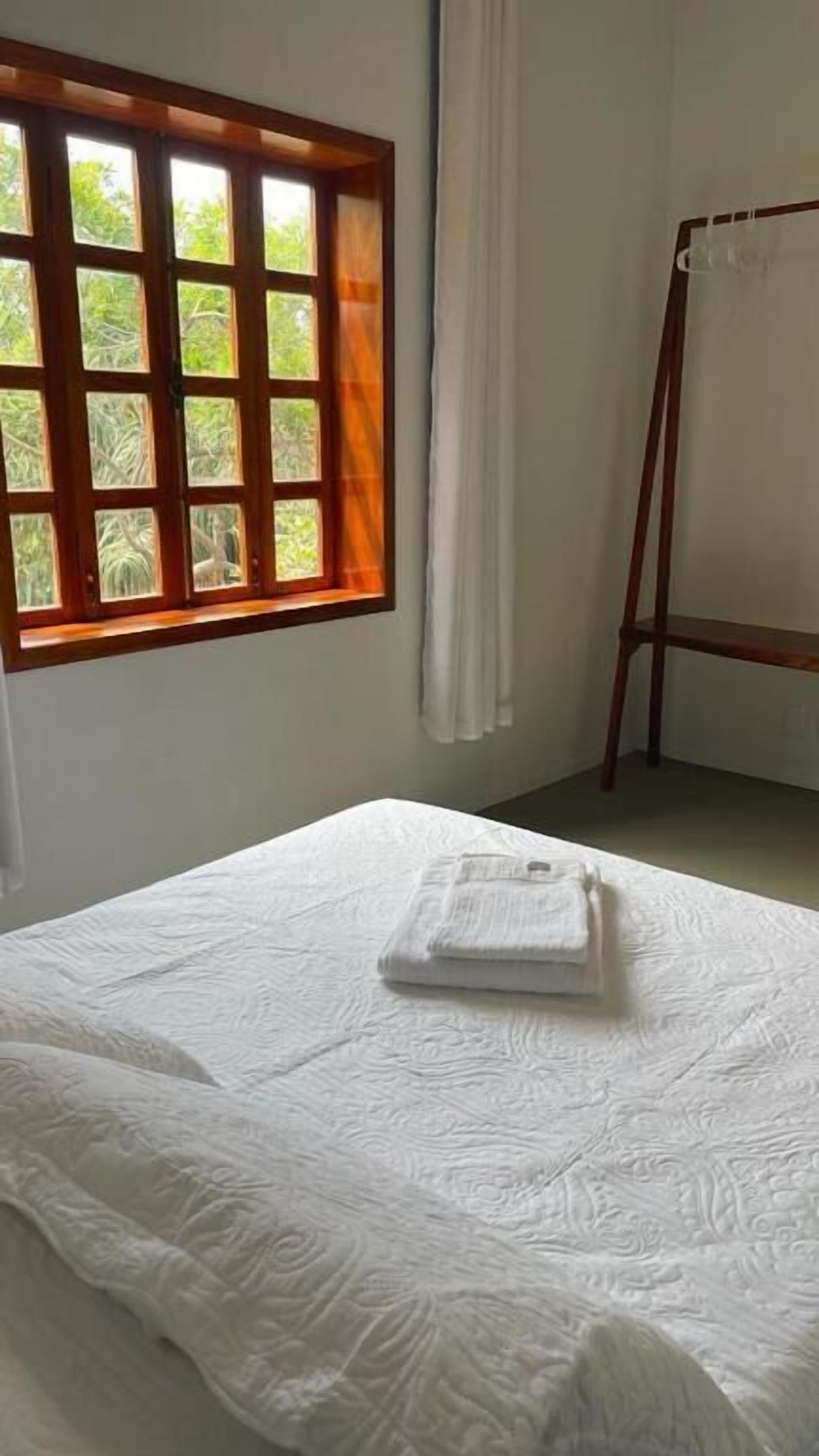 Una habitación con cama, una ventana que da a zonas verdes y un atril de madera con tela blanca.