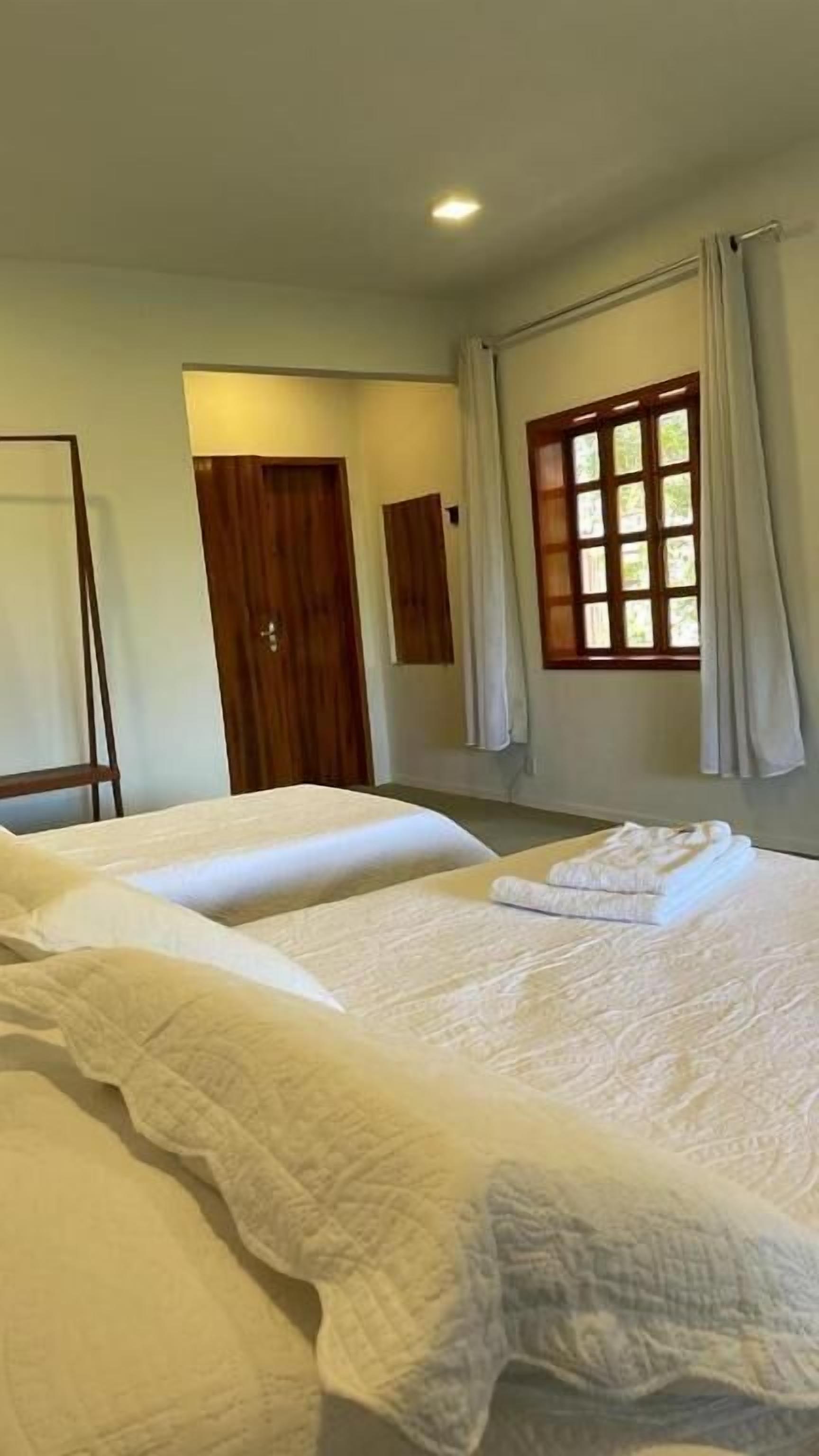 Habitación de hotel con dos camas, una puerta de madera, una ventana con cortinas y una lámpara en el techo.
