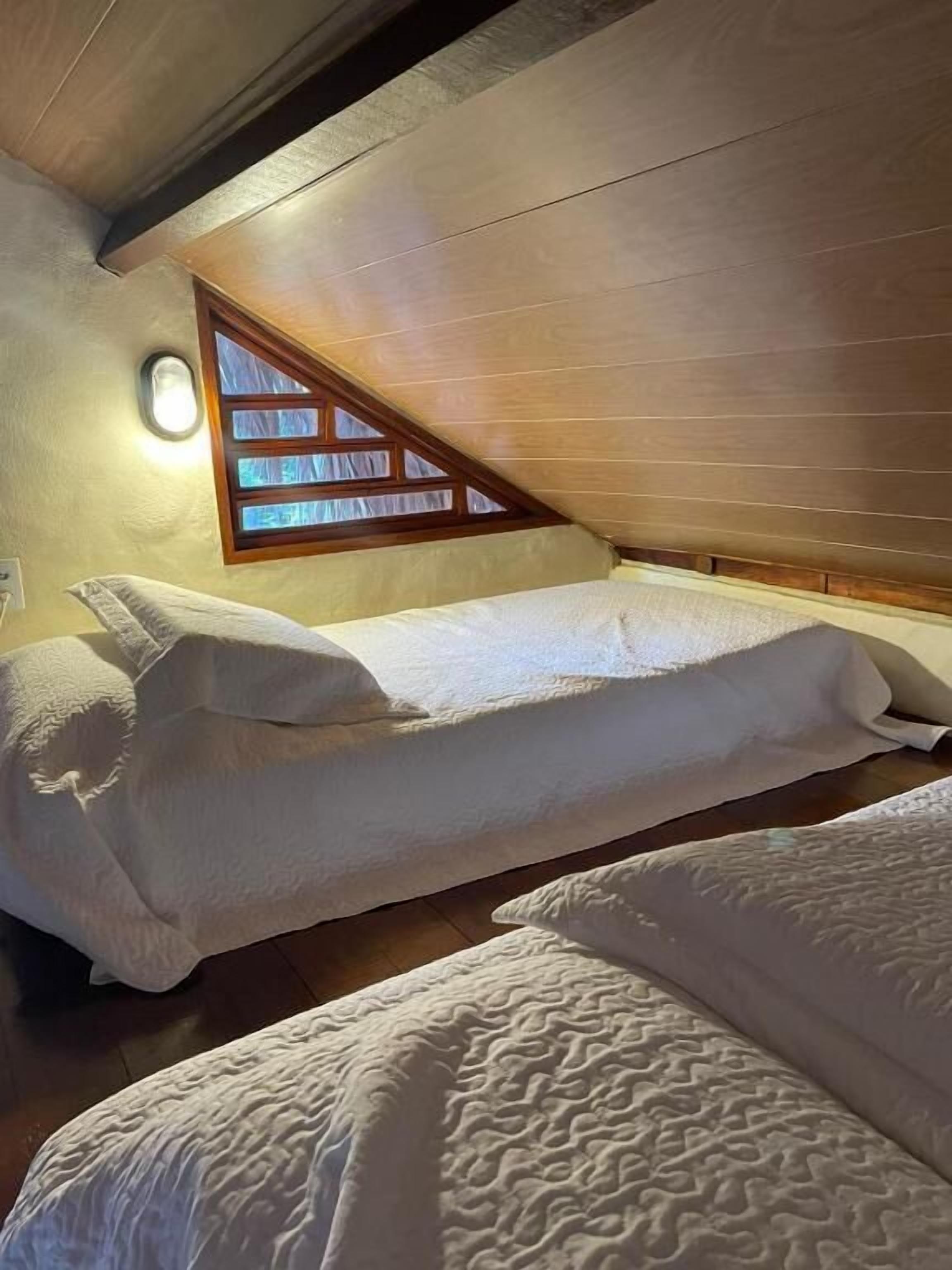 Una habitación pequeña y acogedora con techo inclinado y una ventana. Hay dos camas con ropa de cama blanca.