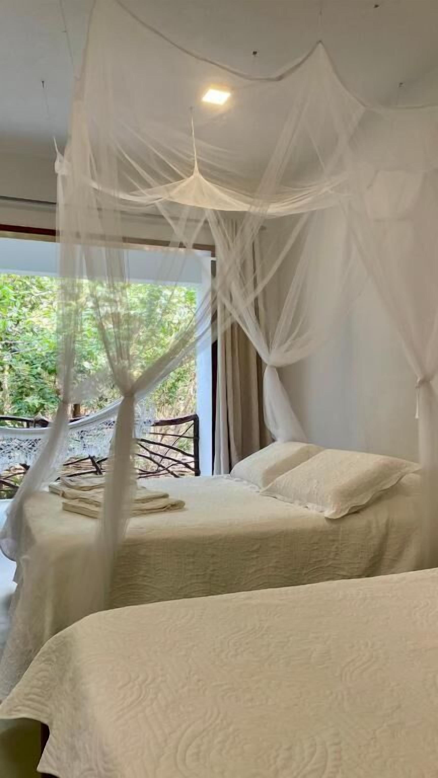 A bedroom with a canopy bed, a view of greenery outside, and a window with curtains.