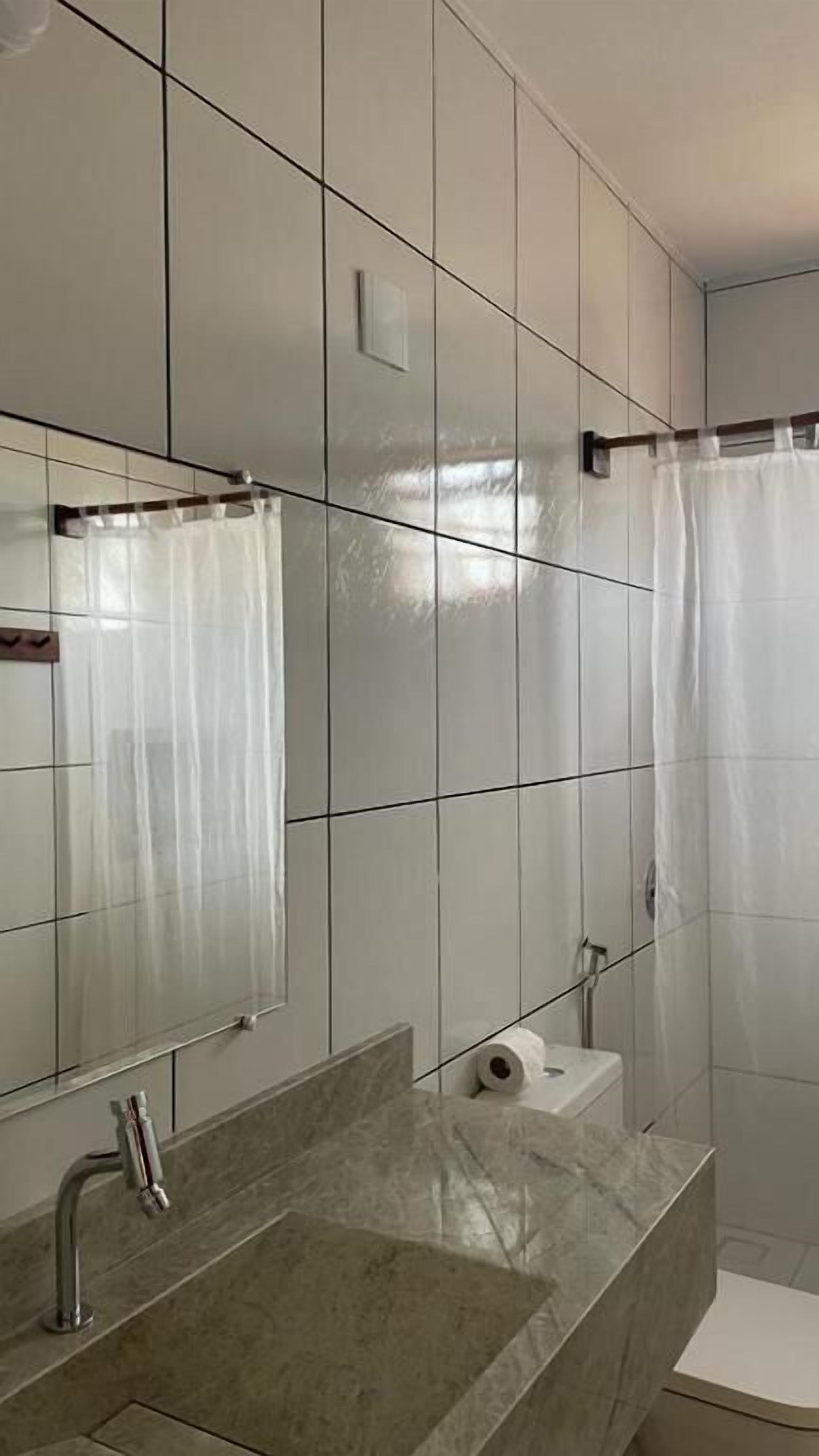 A bathroom with a tiled wall, a sink with a marble countertop, a mirror, a shower curtain, and a toilet.