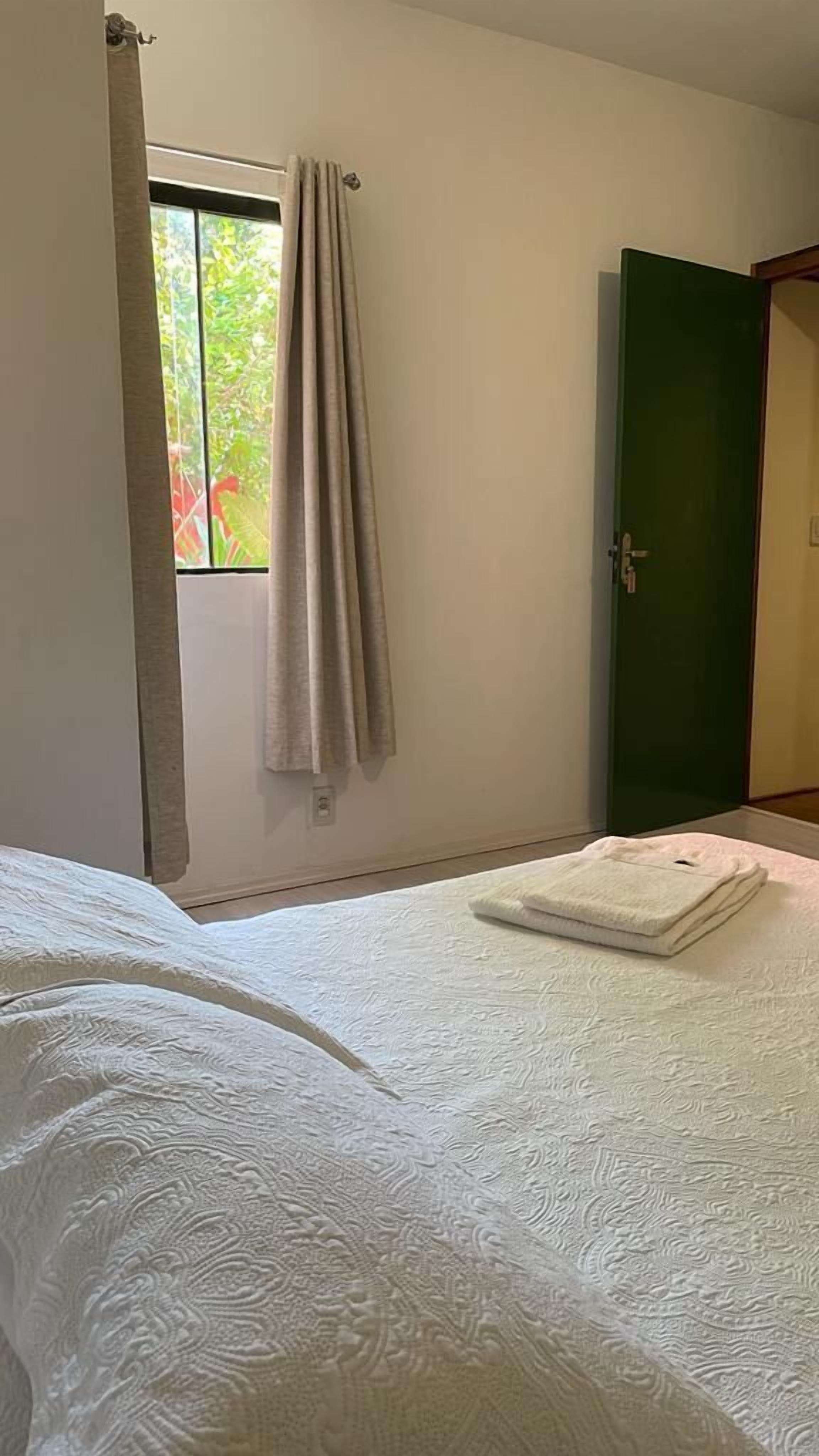 A bedroom with a bed, a window with curtains, and a green door.
