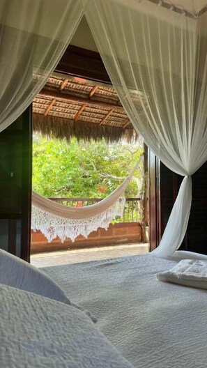 A room with a bed, a hammock, and a view of greenery through a window with white curtains. - CASA B&B (Jijoca de Jericoacoara)