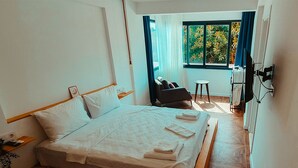 Un lit bien fait, avec du linge de lit et des serviettes blanches, une tête de lit en bois et une petite table de chevet avec une lampe.