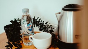 Une table en bois, une cafetière en acier inoxydable, une tasse blanche, une bouteille d’eau et un verre.