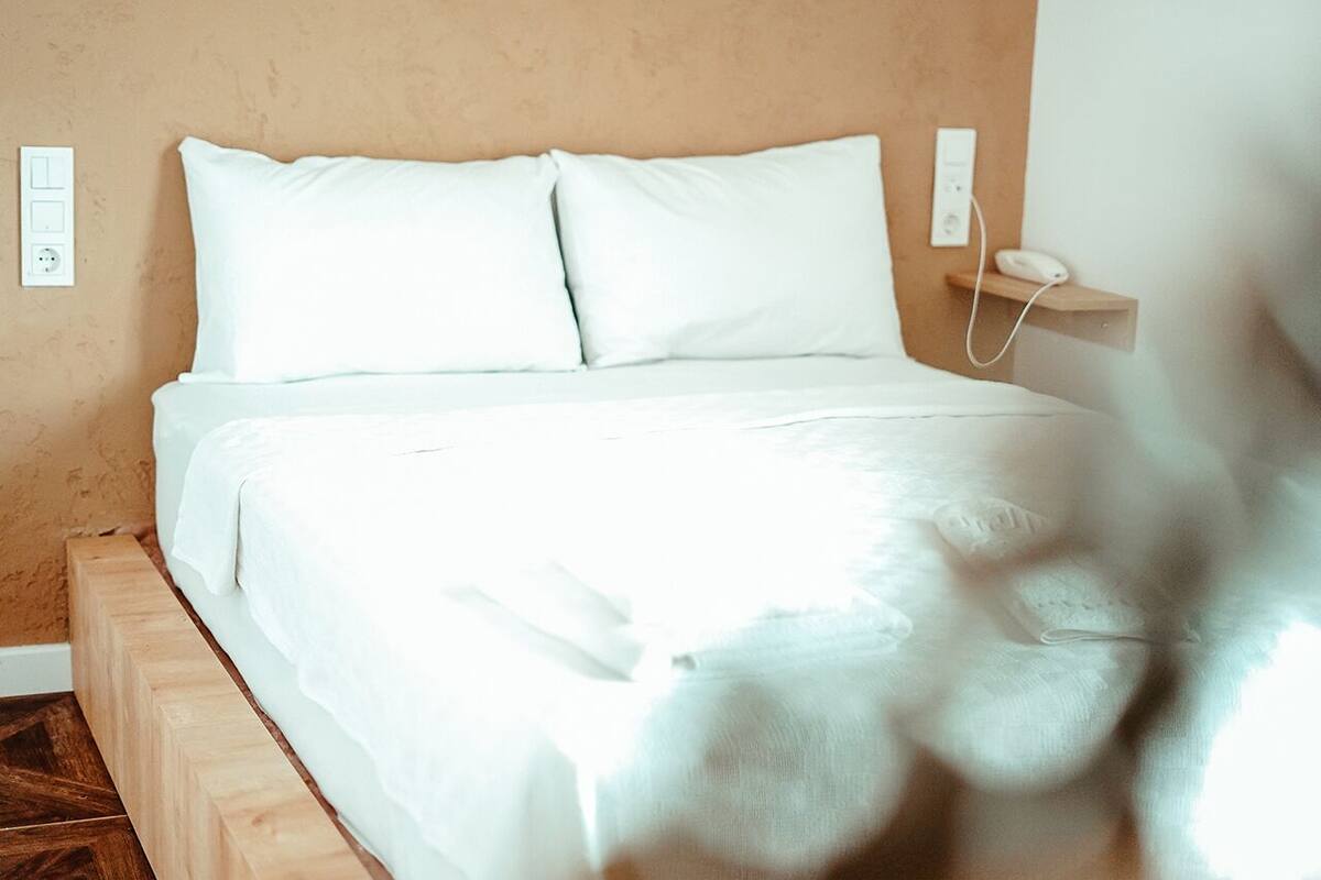 A bed with white bedding in a room with a wooden headboard and a beige wall.