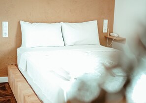A bed with white bedding in a room with a wooden headboard and a beige wall.