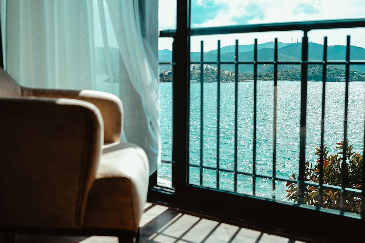A room with a view of a body of water through a window with metal bars.