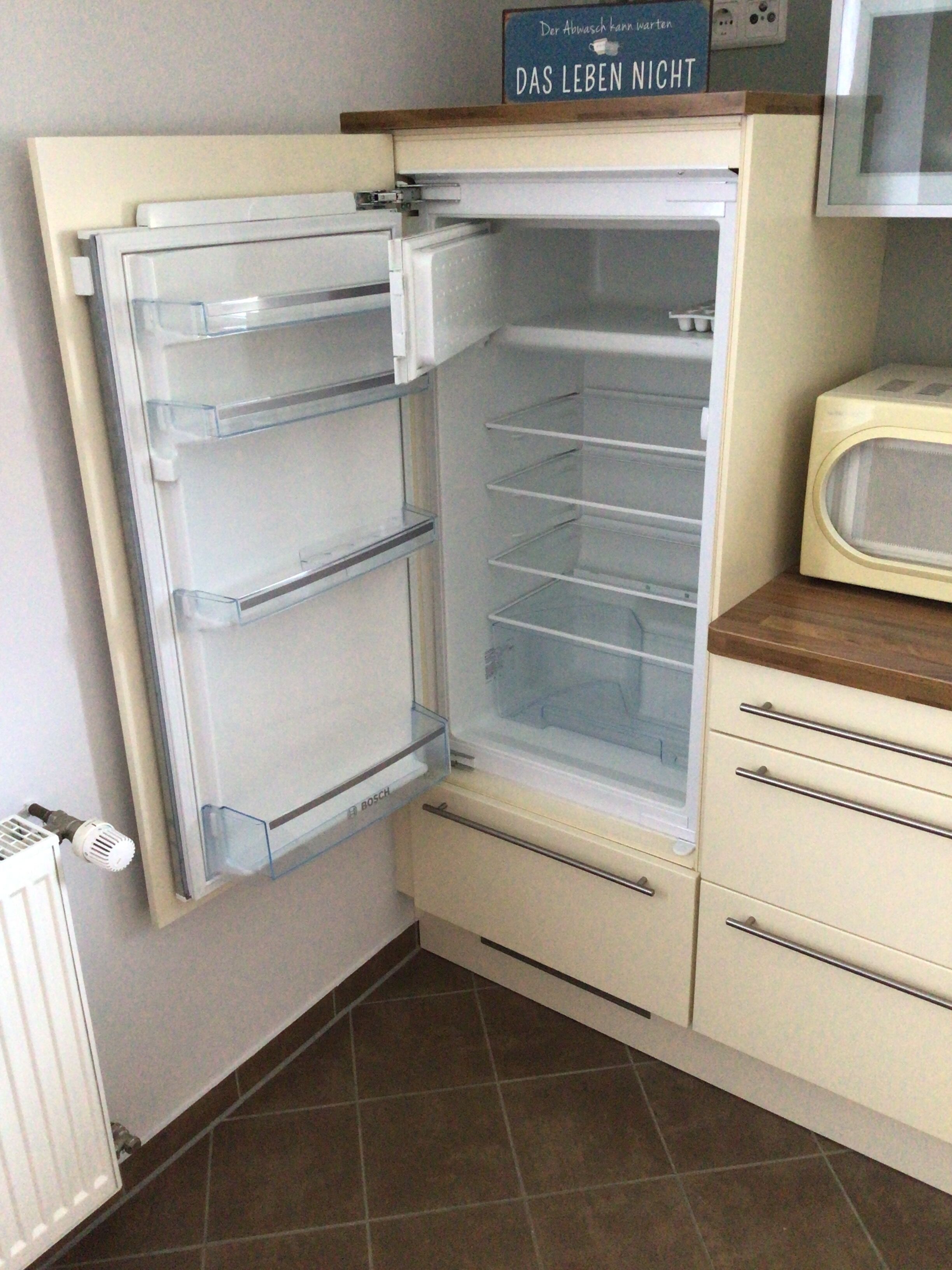 Een open koelkast met meerdere planken, een magnetron op het aanrecht en een bord boven de koelkast.