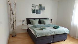 A bedroom with a bed, bedside tables, wall art, and a potted plant.