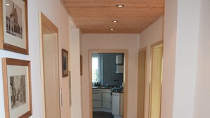 A hallway with wooden flooring and a kitchen in the background.