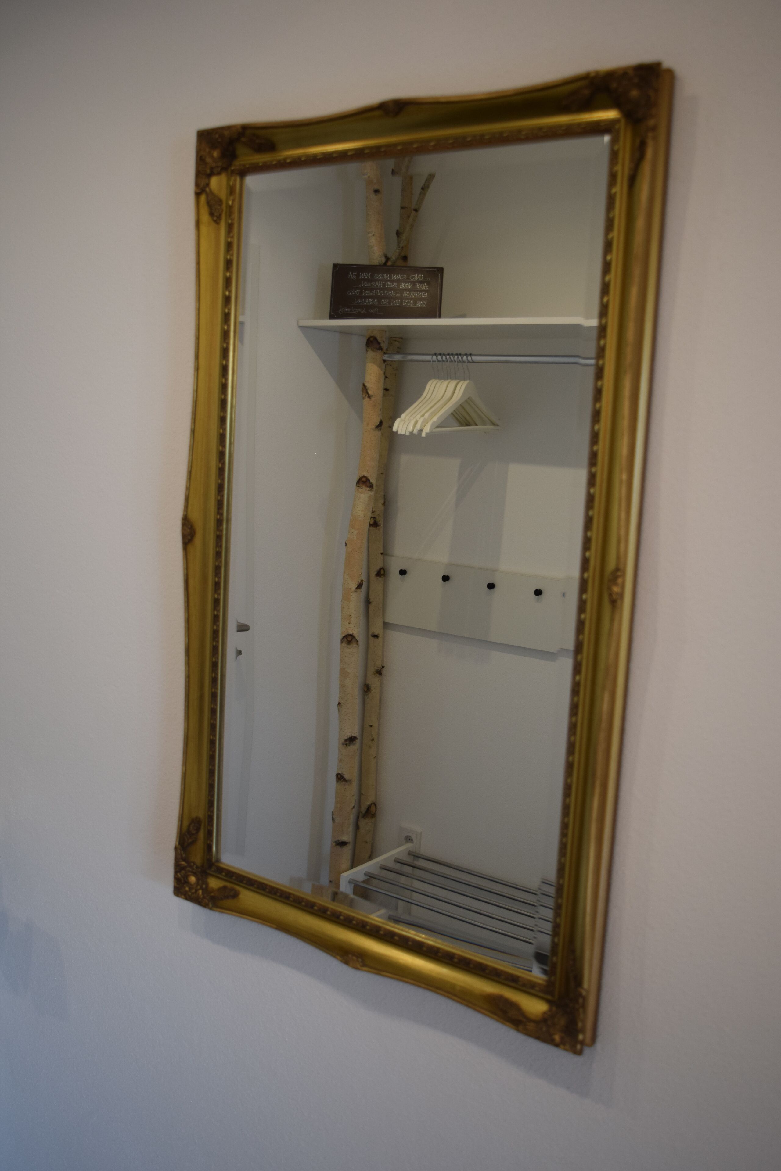 Ein Spiegel mit goldener Rahmung an der Wand befestigt.