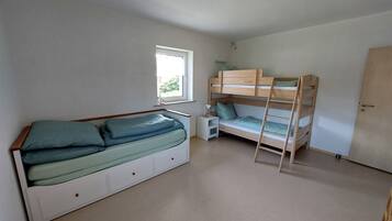 A bedroom with a bunk bed, a single bed, a bedside table with a lamp, and a window.