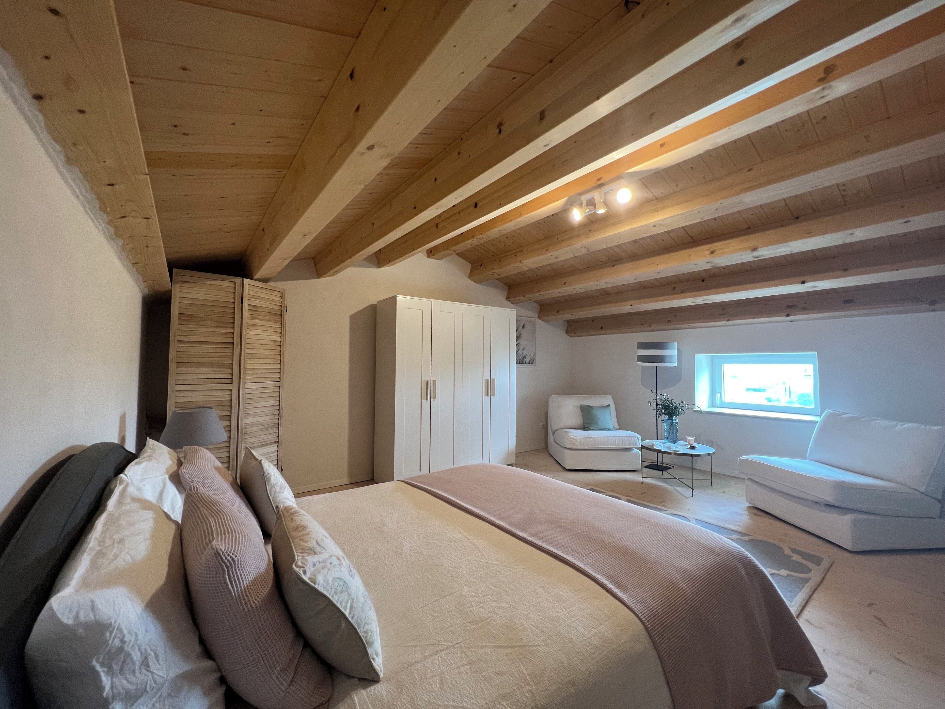A bedroom with a bed, a white wardrobe, a white sofa, and a window with natural light.