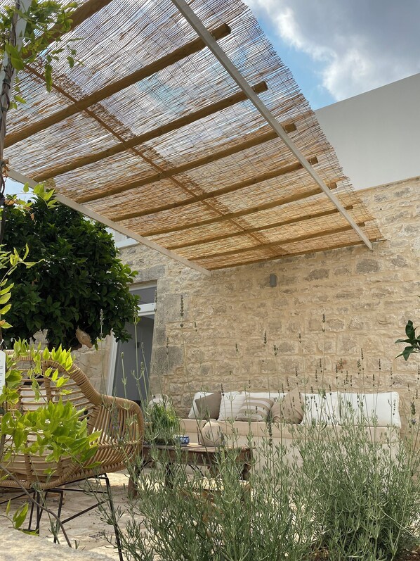Un espacio de estar al aire libre cubierto con un muro de piedra de fondo, techo de tejido y una silla de mimbre.