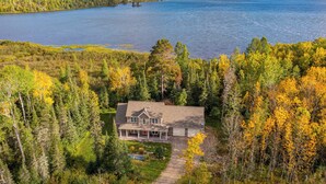A house with a large deck and a view of a lake surrounded by forest.