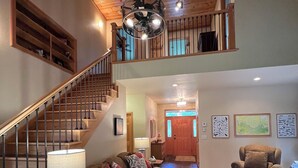 A spacious living room with a high ceiling, wooden staircase, and a view of the upper floor.