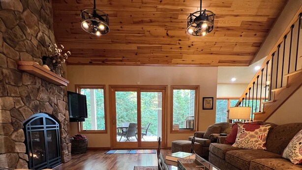 A spacious living room with a stone fireplace, wooden flooring, a large sofa, and a staircase leading to an upper level.