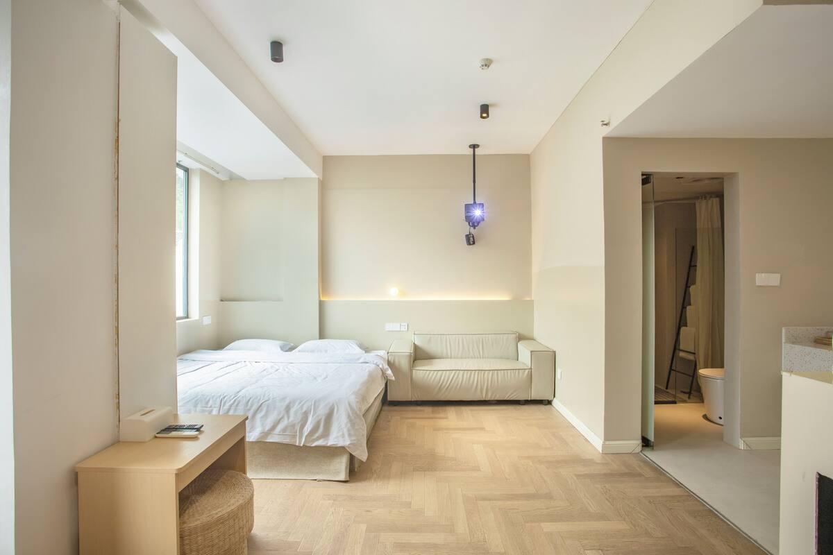 A modern bedroom with a bed, a sofa, a bedside table, and a window.