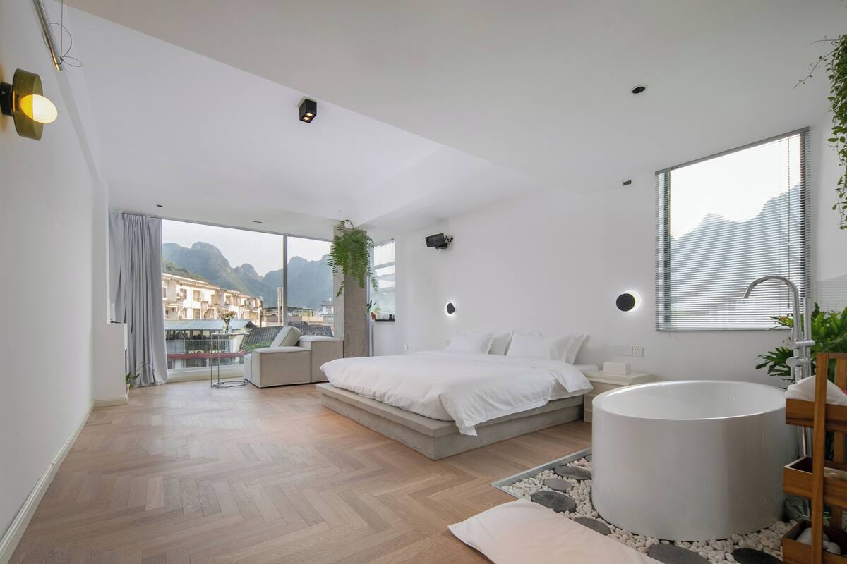 A modern bedroom with a large bed, a bathtub, and a view of the city.