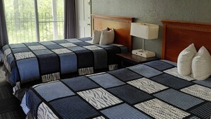 Ein Hotelzimmer mit zwei Betten, einem Nachttisch, einer Lampe und Blick auf Grünflächen.
