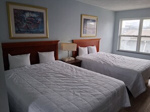 Een hotelkamer met twee bedden, een nachtkastje met een lamp en twee ingekaderde foto's aan de muur.