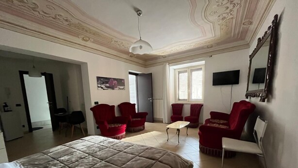 A hotel room with a large bed, two red armchairs, a small table, and a TV mounted on the wall. - Lercarappart 1 (Lercara Friddi)