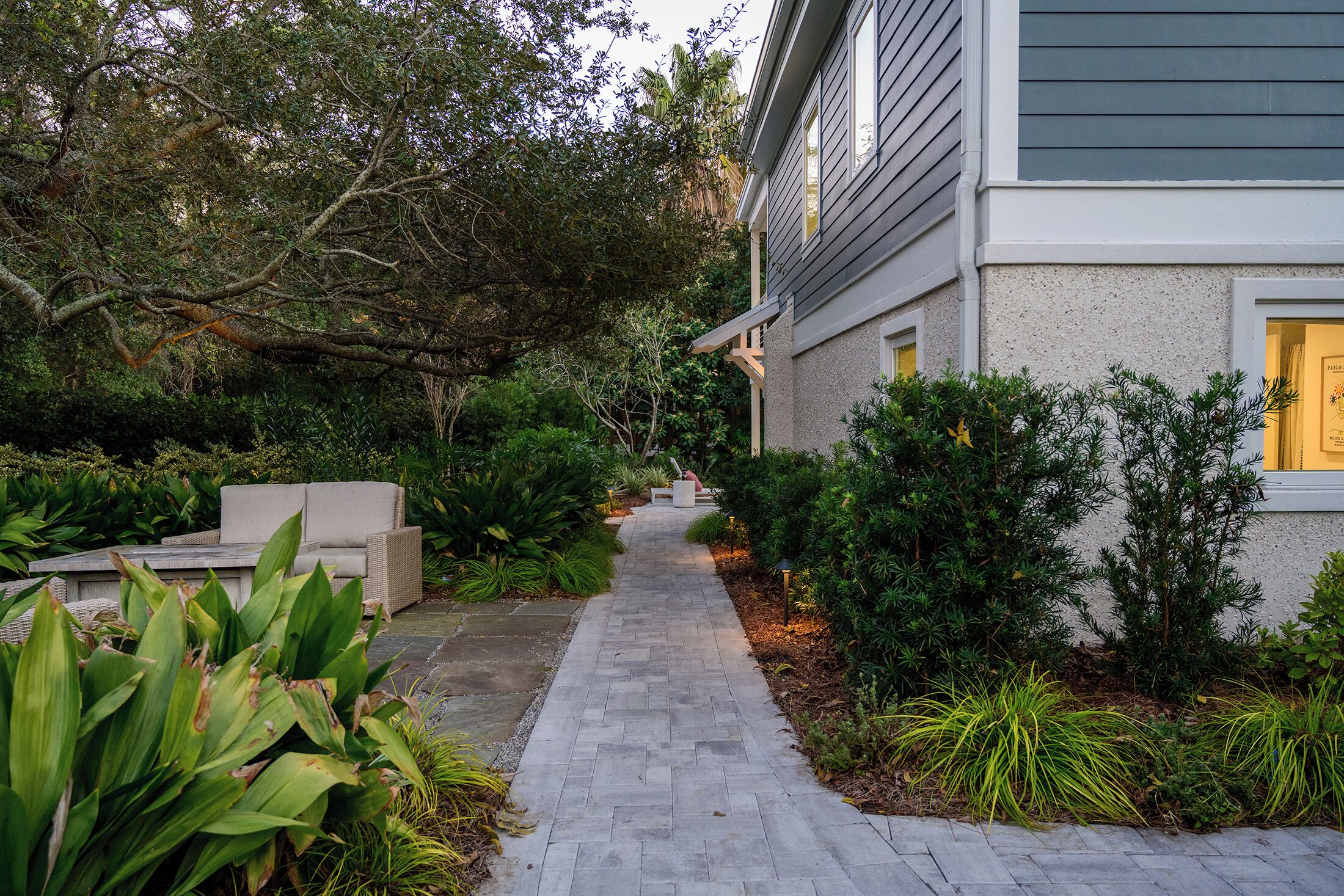 A paved pathway leading to a house with a grey exterior and a white door.