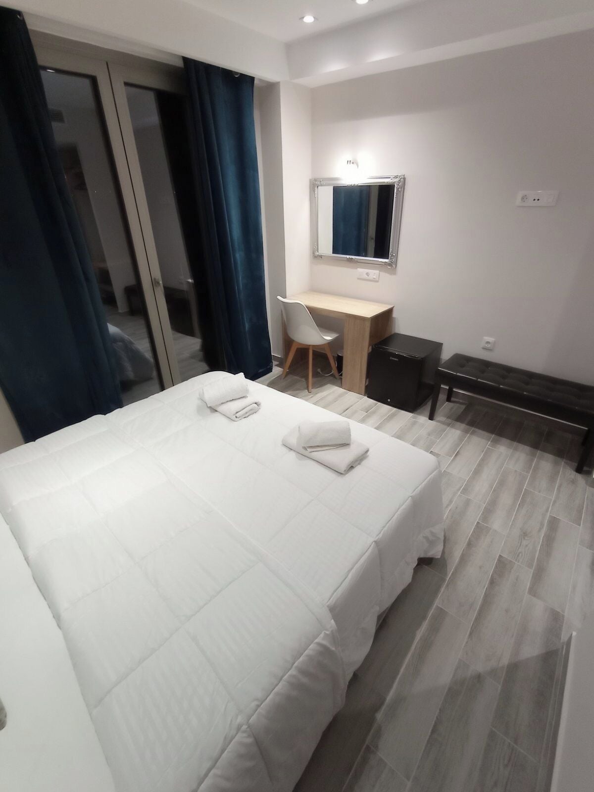 A hotel room with a large bed, a desk, a chair, and a bench.