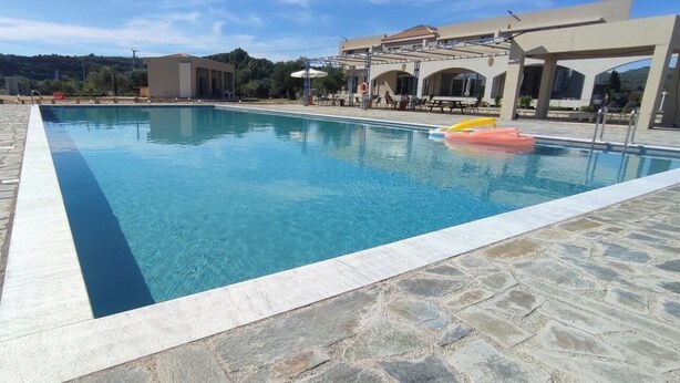 A swimming pool with stone tiles, a lifebuoy, and a covered area with tables and chairs. - Vians Olympia Resort (Pyrgos)