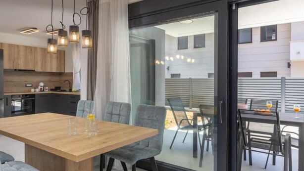 Eine moderne Küche mit Holzausstattung und einem Essbereich mit Glastür zum Außenbereich.